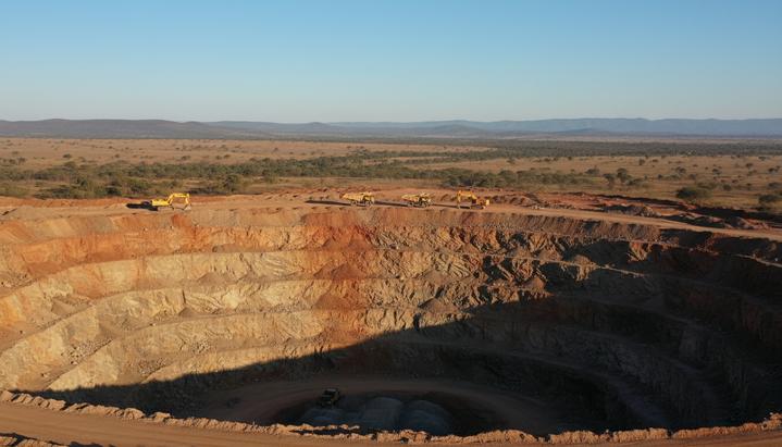 Карьер золотодобывающего рудника на ранней стадии разработки, террасы рудника и тяжелая техника на фоне саванны.