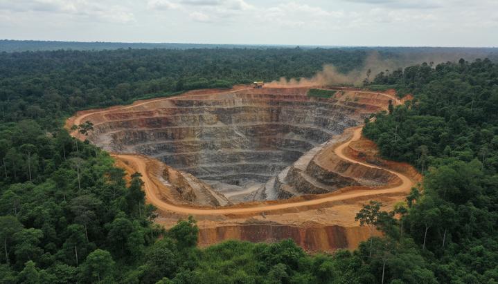 Панорама огромного никелевого карьера с террасами и красно-коричневой почвой в Индонезии. Вдали видна тяжелая техника на фоне тропического леса.