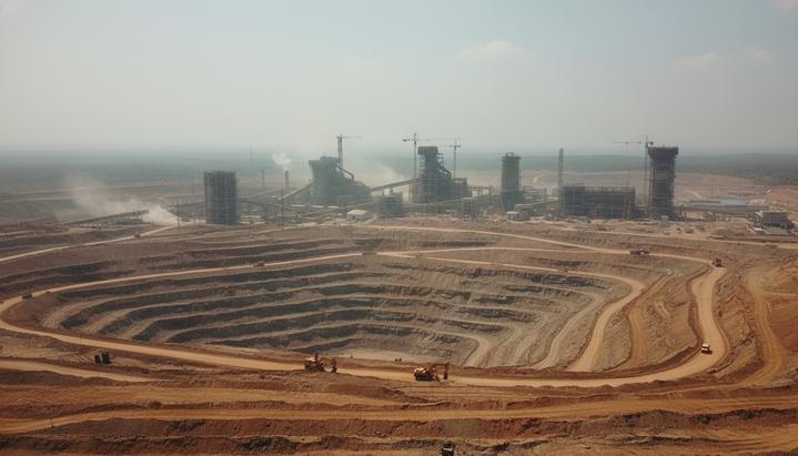 Огромный карьер по добыче никелевой руды в Индонезии на фоне строящихся промышленных корпусов нового металлургического завода.