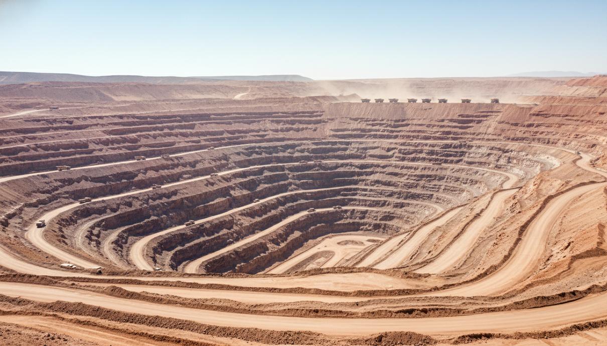 Вид на огромный открытый медный рудник в пустыне Атакама, Чили. Террасы шахты, красная земля, горные породы и крупная техника без людей.